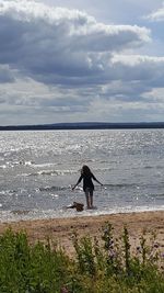 Man with dog standing on beach against sky