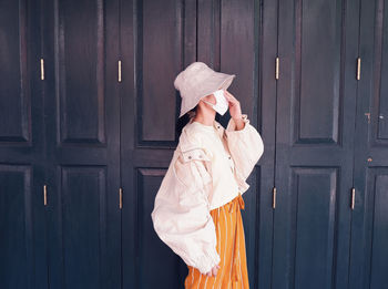 Woman wearing hat standing against door