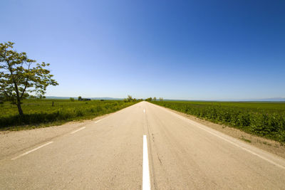 Road amidst field against clear sky