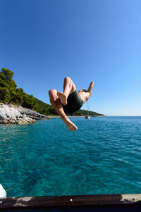 Shirtless man jumping in sea against clear blue sky