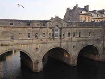 Arch bridge over river by buildings against sky