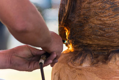 Cropped image of man using blow torch on wooden sculpture