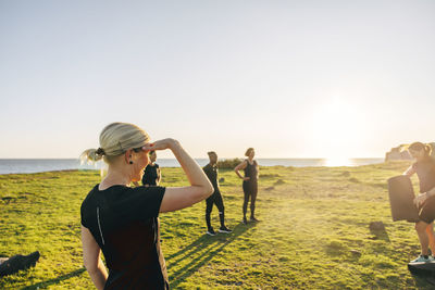 Woman shielding eyes during group training on sunny day at beach