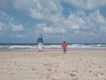 Rear view of father and son walking on sandy beach