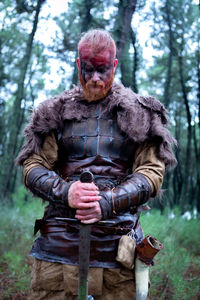 Warrior with sword standing against trees in forest