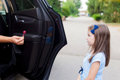 Cropped hand of person giving chocolate to girl standing on road