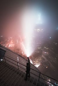 Man standing on illuminated railing against sky at night