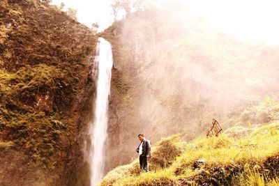 Low angle view of man standing against waterfall on hill