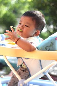 Cute baby boy eating food while sitting in stroller