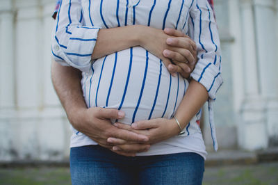 Midsection of pregnant woman with husband standing against wall