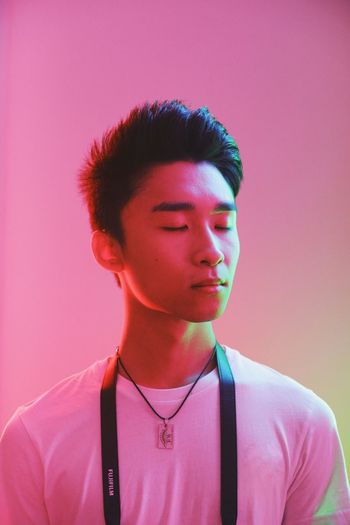 Young man standing against pink background