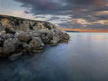 Rocks on sea shore against sky during sunset