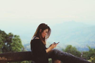 Young woman using mobile phone against sky