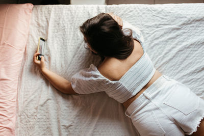 Rear view of young woman taking selfie with mobile phone while lying on bed at home