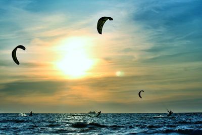 People kiteboarding at sea against sky during sunset