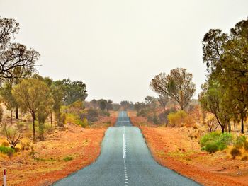 Empty road amidst trees against clear sky