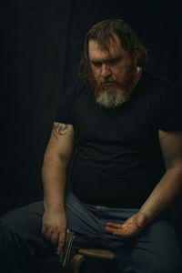 Portrait of senior man playing guitar while sitting against black background