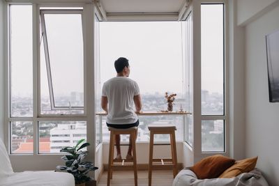 Rear view of man looking through window