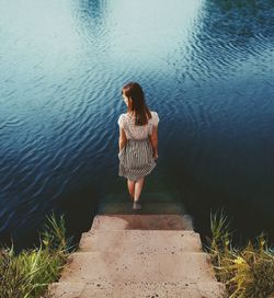 Rear view of young woman standing on steps by lake