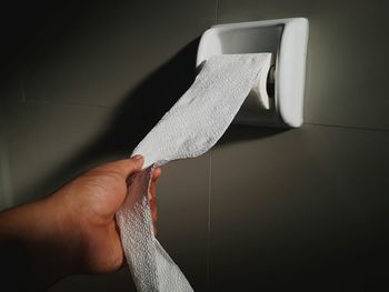 Close-up of human hand holding toilet paper against wall in bathroom