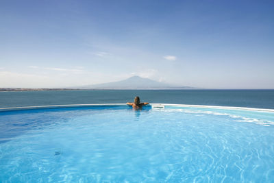 Adult woman relaxing in infinity pool looking at horizon with mount etna