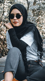 Portrait of young woman wearing sunglasses sitting outdoors