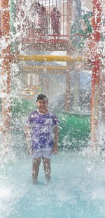 Portrait of smiling boy standing amidst splashing water