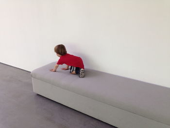 Full length of boy kneeling on sofa against wall at home