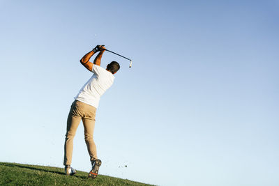 Professional male golf player preparing to hit ball with putter in green field while looking away on summer day