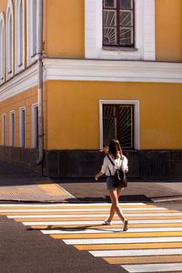 Rear view of woman crossing street against building in city