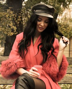 Young woman with coffee cup sitting on bench in park