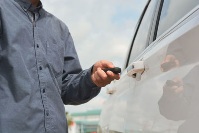 Rear view of man holding mobile phone while standing by car