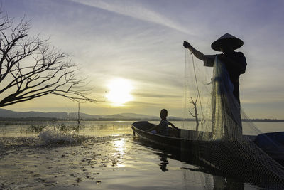 Silhouette men on lake against sky during sunset