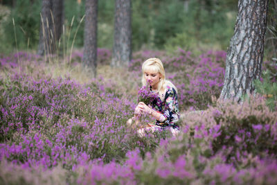 Woman sitting by tree amidst purple flowering plants in forest