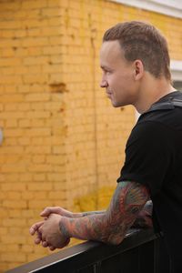 Side view of man sitting against brick wall