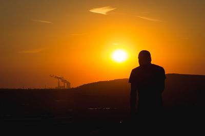 Silhouette of man looking at distant power plant
