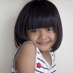 Portrait of cute smiling girl with bangs against wall