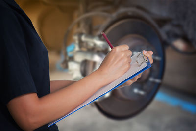 Midsection of woman writing while standing in garage