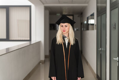 Portrait of woman wearing graduation gown standing against building