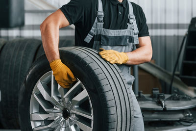 Walking and holding tyre. man in uniform is working in the auto service.