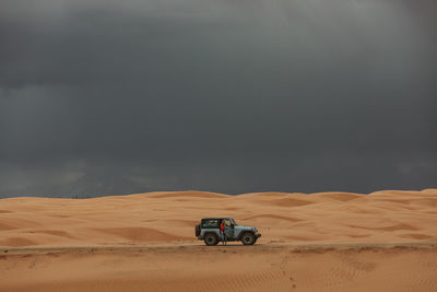Woman and her jeep while driving across sand dunes under stormy skies