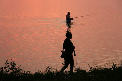 Rear view of silhouette man standing against orange sky