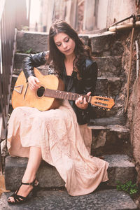 Young woman playing guitar against wall