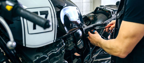 Midsection of mature mechanic repairing motorcycle in garage