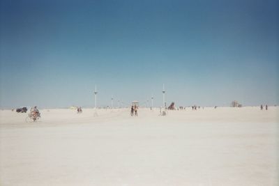 People on sand against clear blue sky