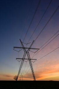 Low angle view of electricity pylon against sky during sunset