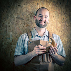 Portrait of smiling man holding work tool while standing against wall