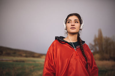 Beautiful young woman wearing headphones while standing on field against sky