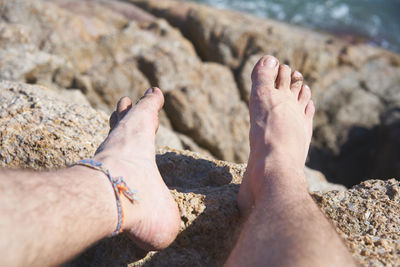 Low section of man relaxing on rock at beach