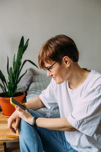 Woman with short hair at home sitting on the floor with her smartphone